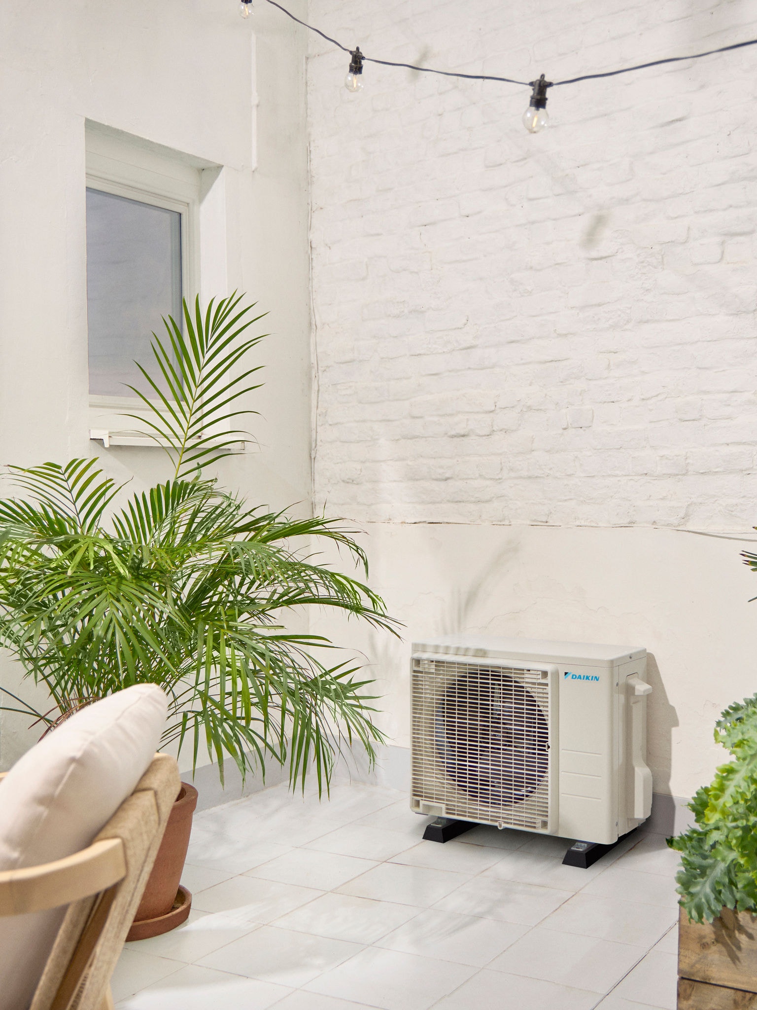 Unitate exterioară Daikin pe terasă albă cu o plantă