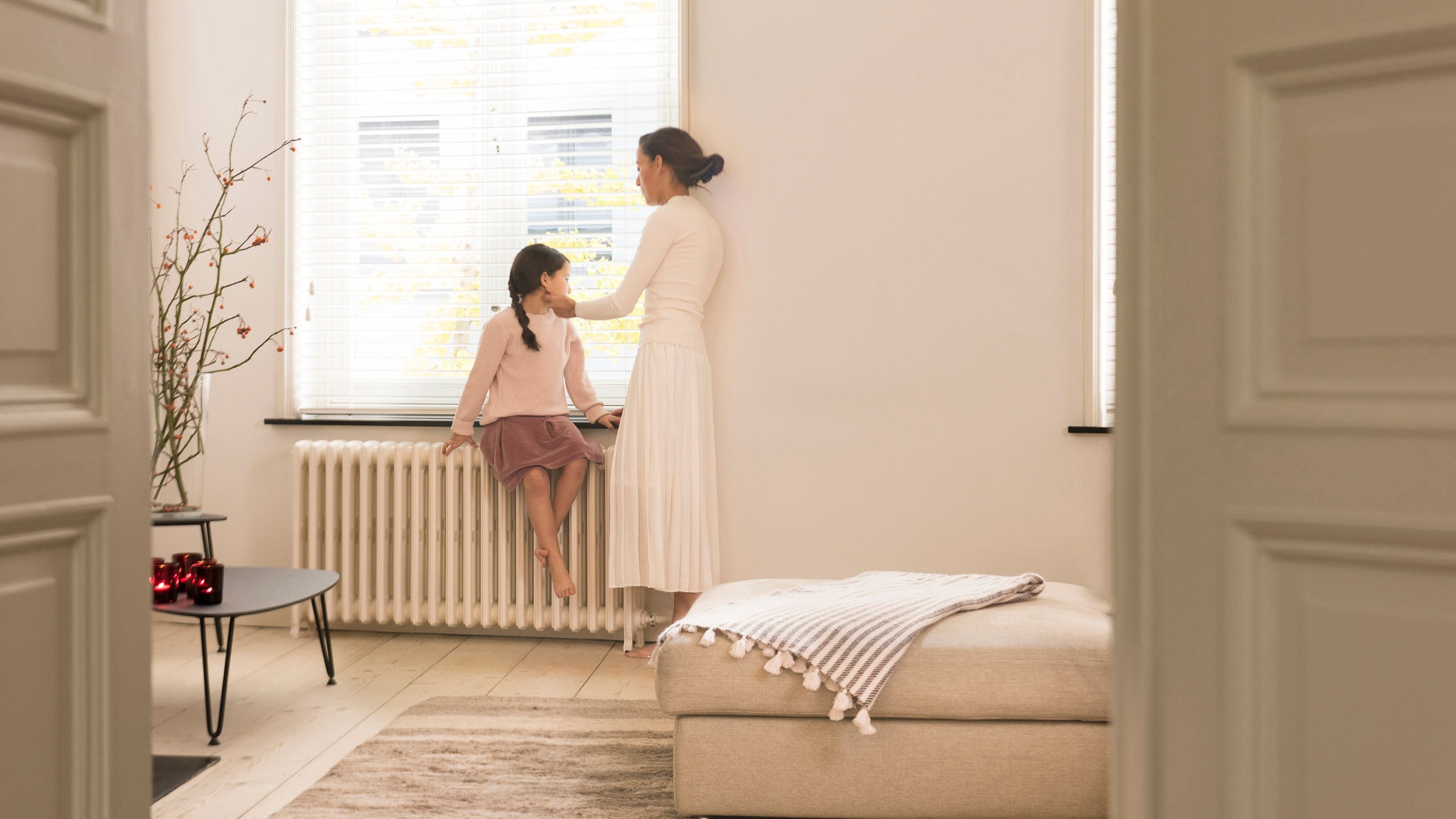 Mama și fiica privind afară pe fereastră din camera de zi perfect încălzită