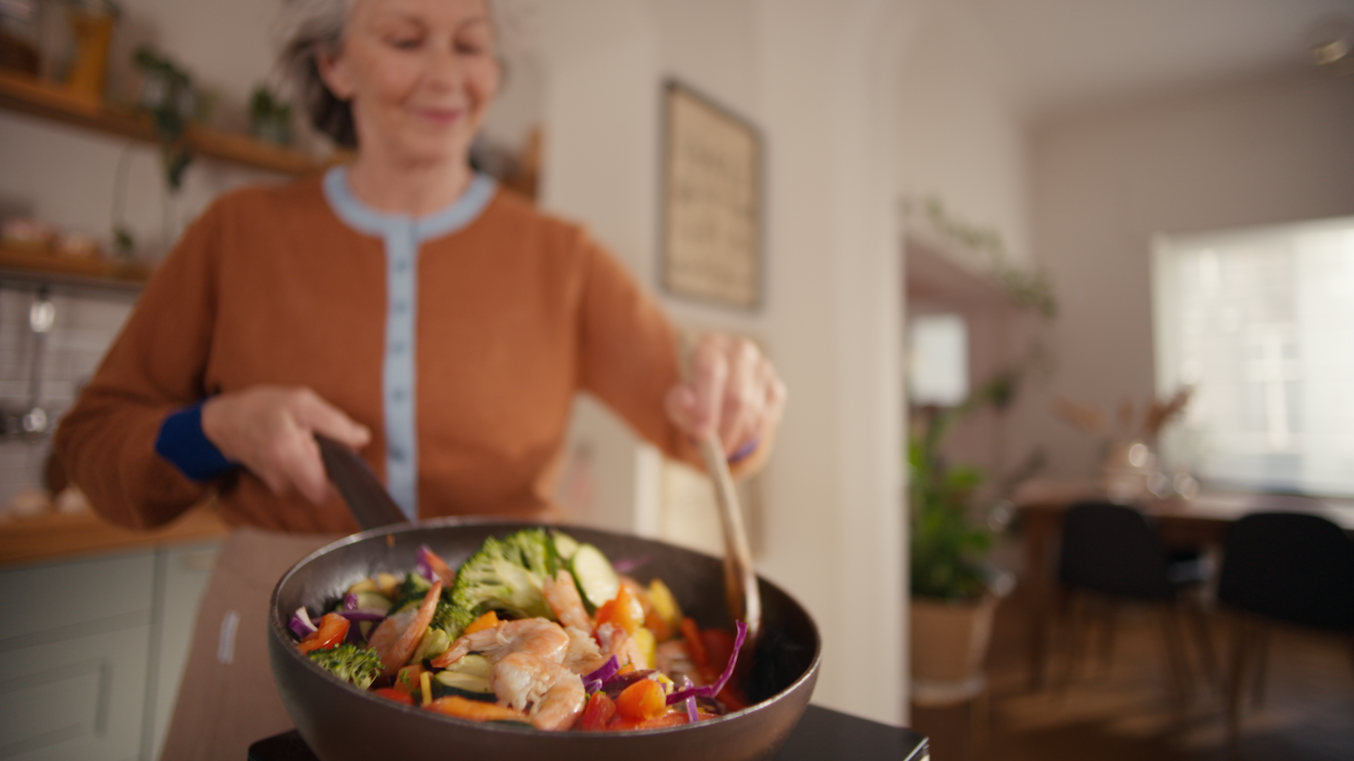 Femeie zâmbind, preparând creveți la tigaie, generând mirosuri specifice în bucătărie