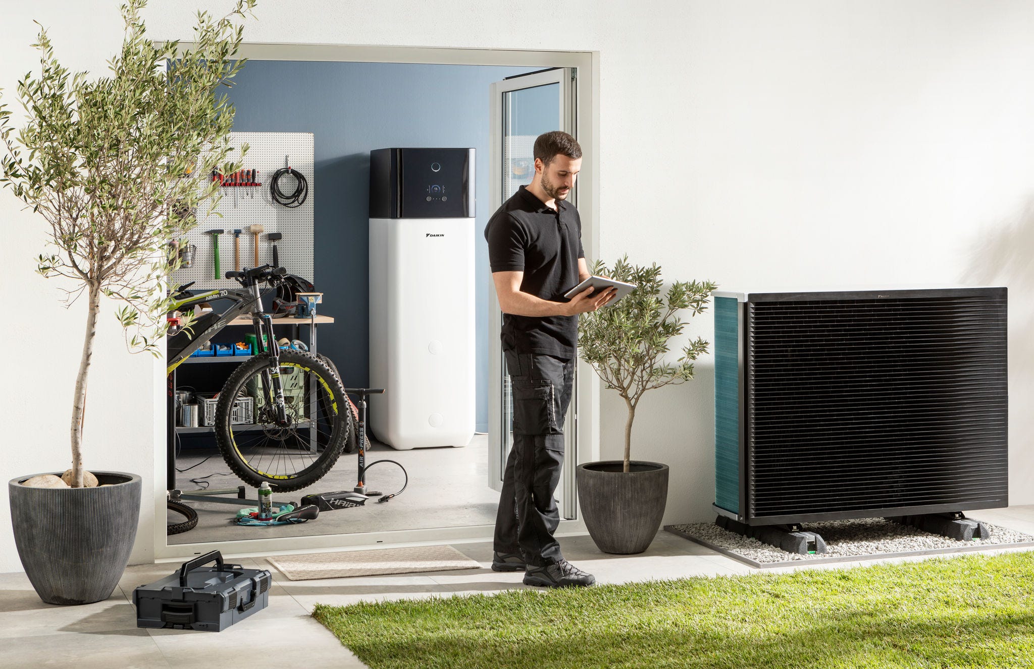 Instalator care verifică unitatea exterioară a pompei de căldură cu sursă de aer și rezervorul de apă caldă