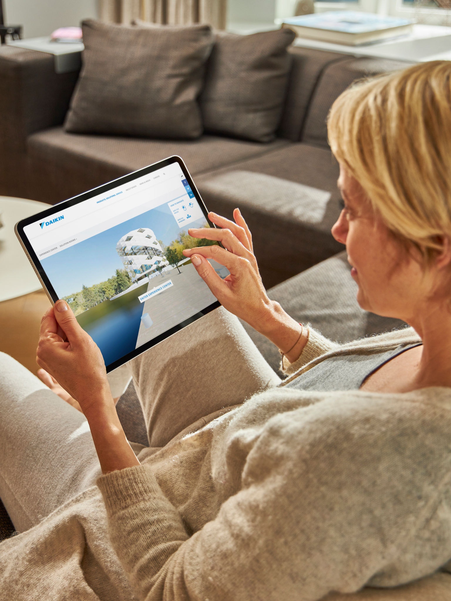 Femeie stând pe canapea și observând aparate de aer condiționat în centrul virtual de experiențe pe laptop