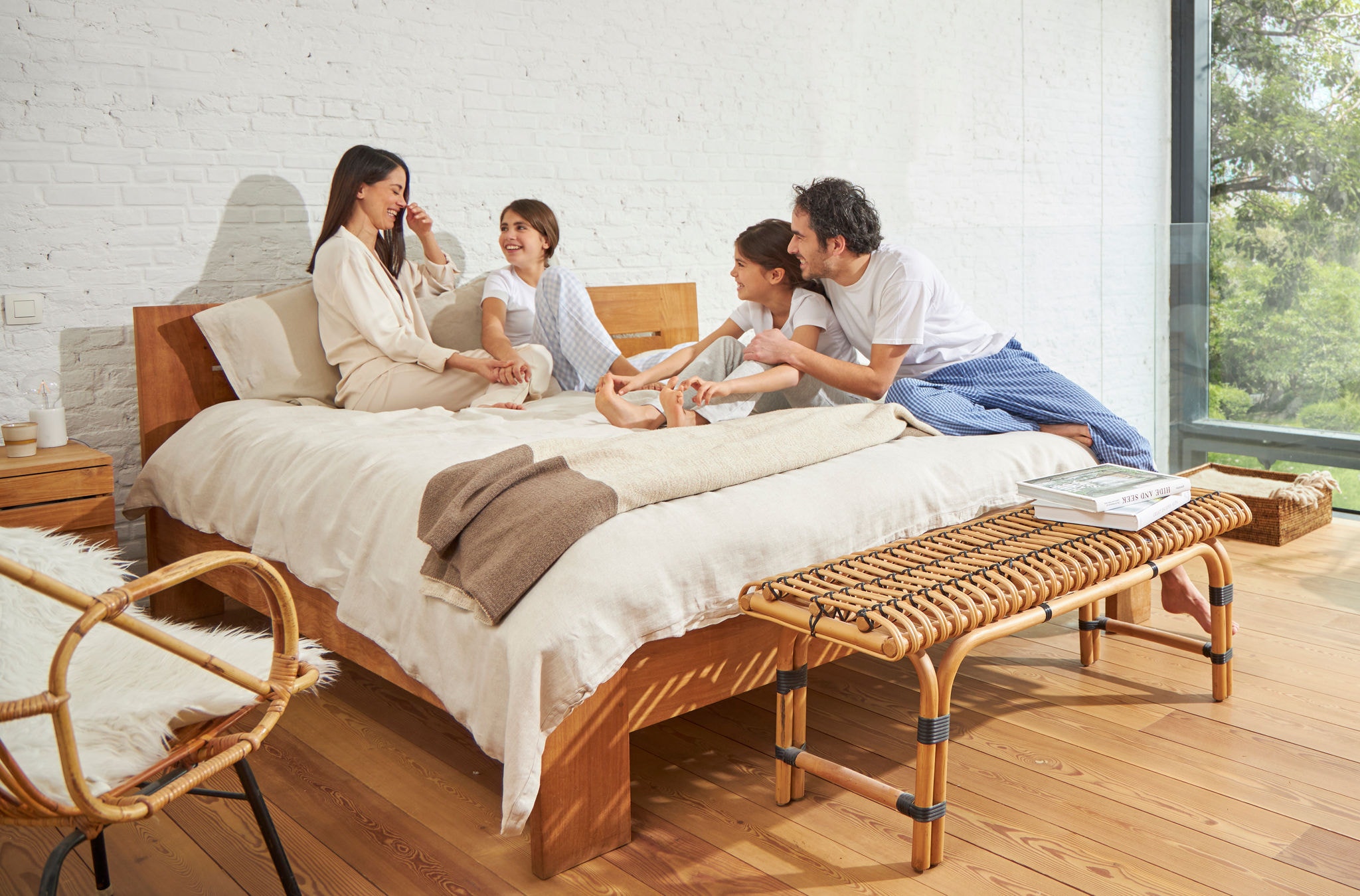 O femeie și un bărbat stând pe un pat cu două fetițe, relaxați, râzând și bucurându-se de aer sănătos.