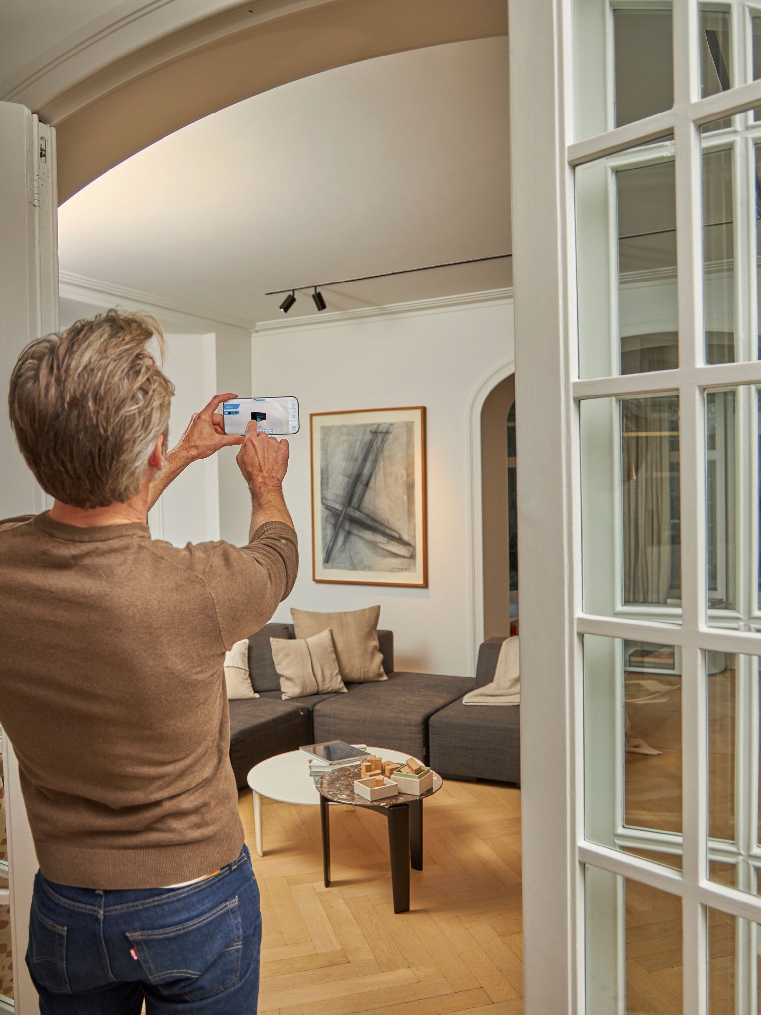 Bărbat care utilizează aplicația 3D cu pompe de căldură aer-aer și realitate îmbunătățită pentru a vizualiza unitățile într-un context de design interior și exterior