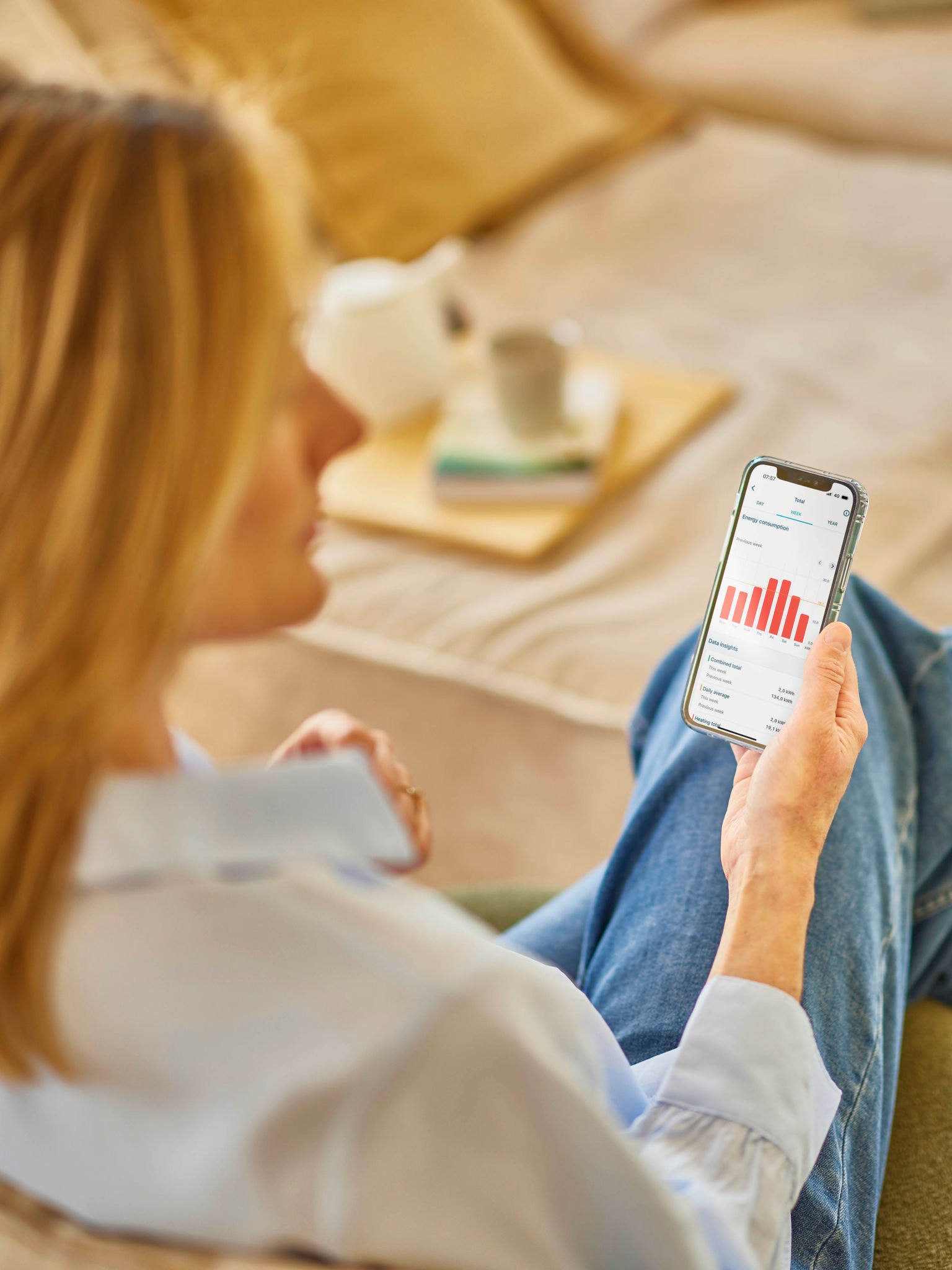 O femeie cu păr blond își consultă consumul de energie din aplicația de pe telefonul mobil