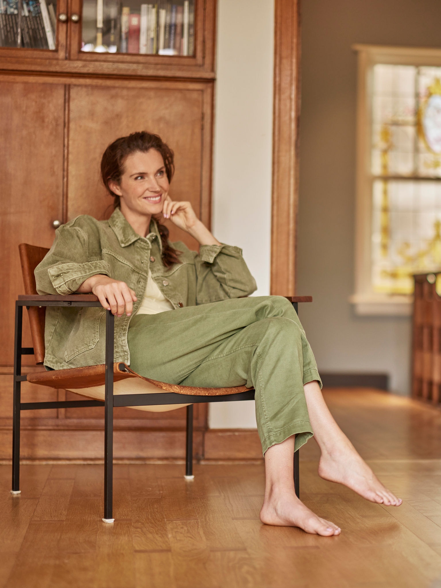 Femeie stând într-un fotoliu, desculță, zâmbind și privind înainte