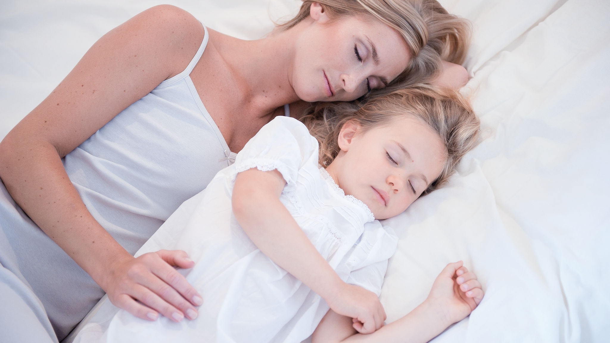 Mama și fetița dormind una lângă cealaltă într-un pat alb și aer curat