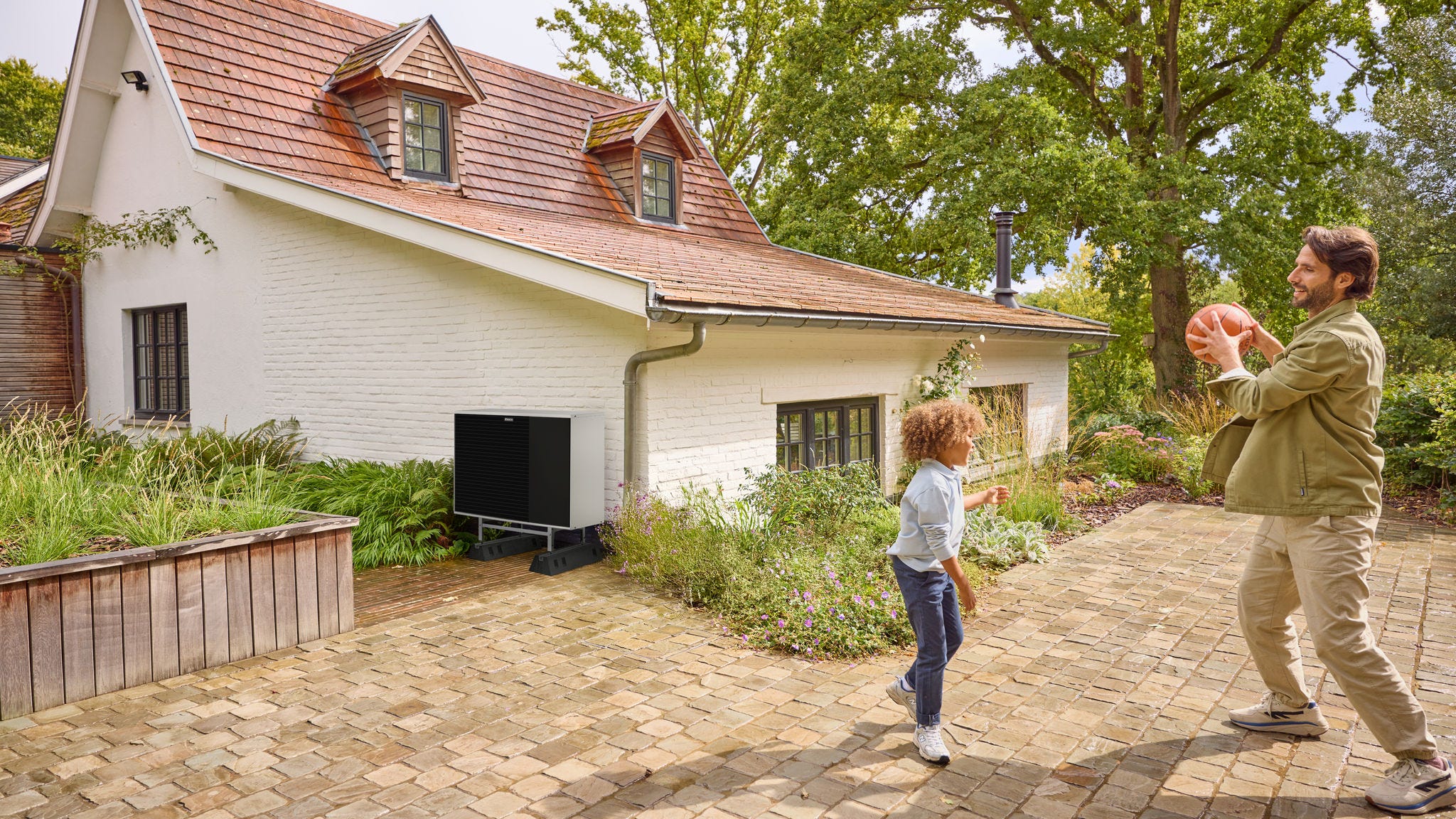 Tată jucându-se cu mingea împreună cu copilul său în curte, lângă o pompă de căldură instalată în apropiere