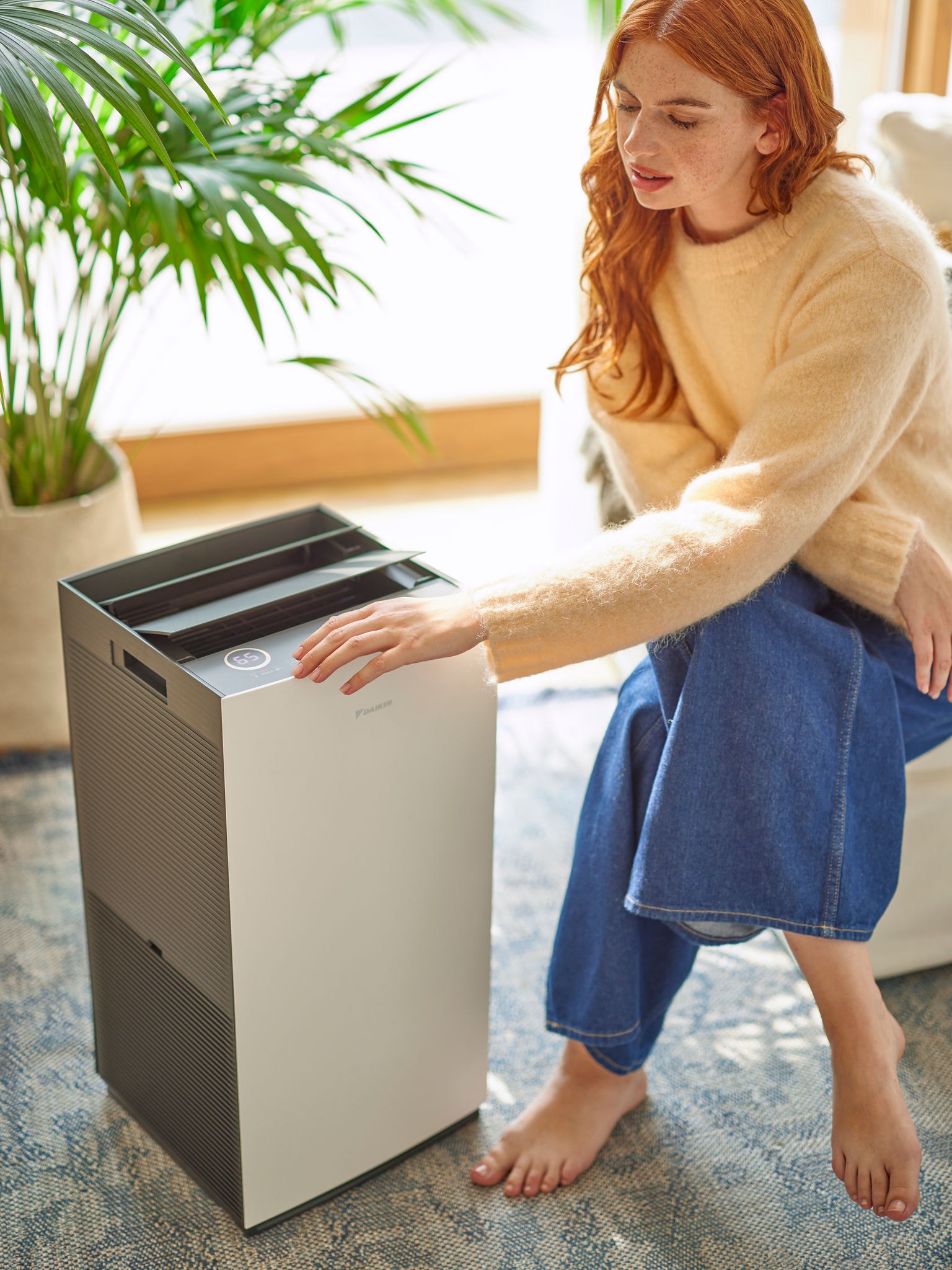 Femeie în camera de zi, reglând comenzile unui purificator de aer Daikin