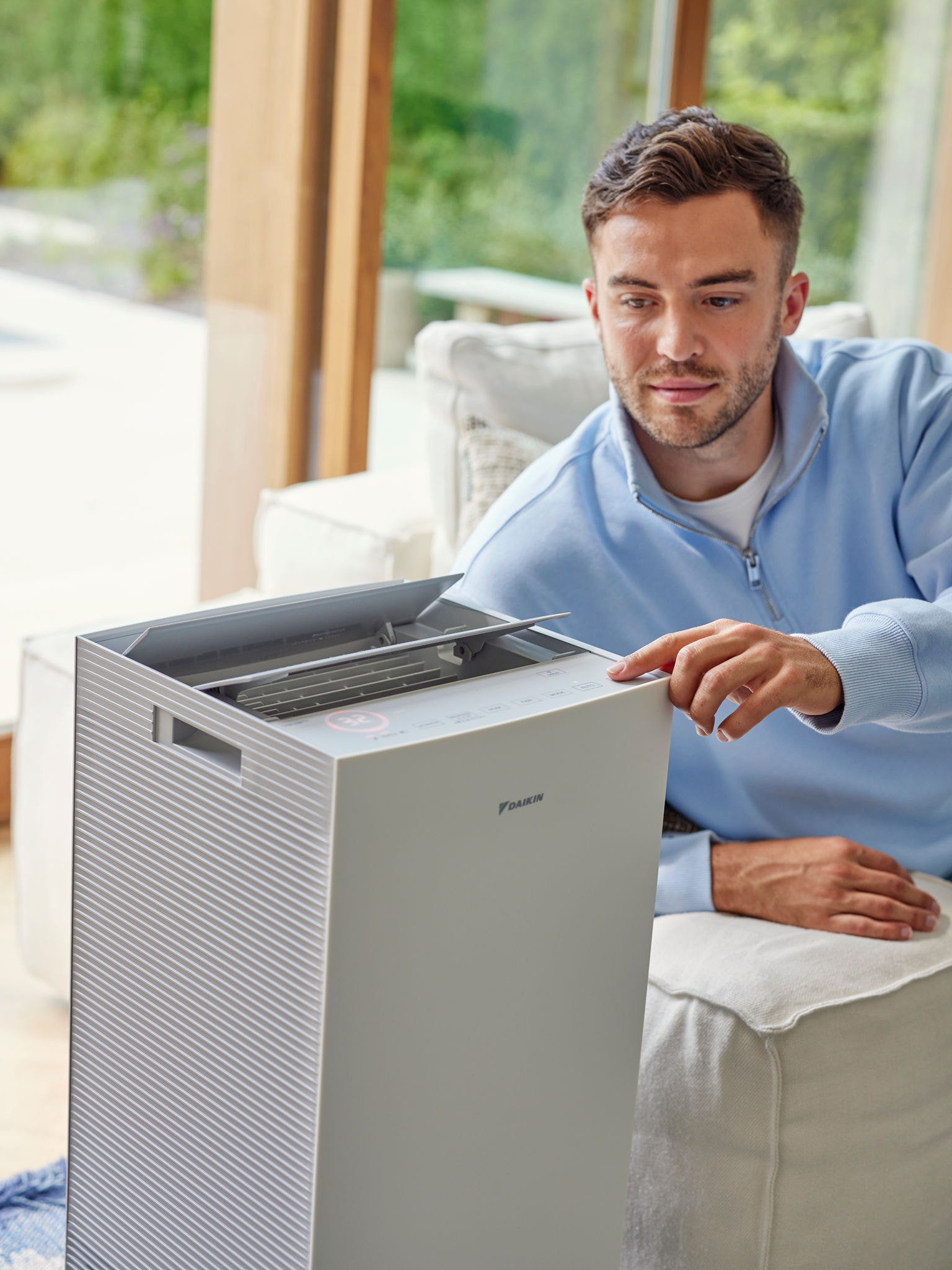 Bărbat reglând un purificator de aer Daikin în living, pentru a reduce alergenii proveniți de la pisică