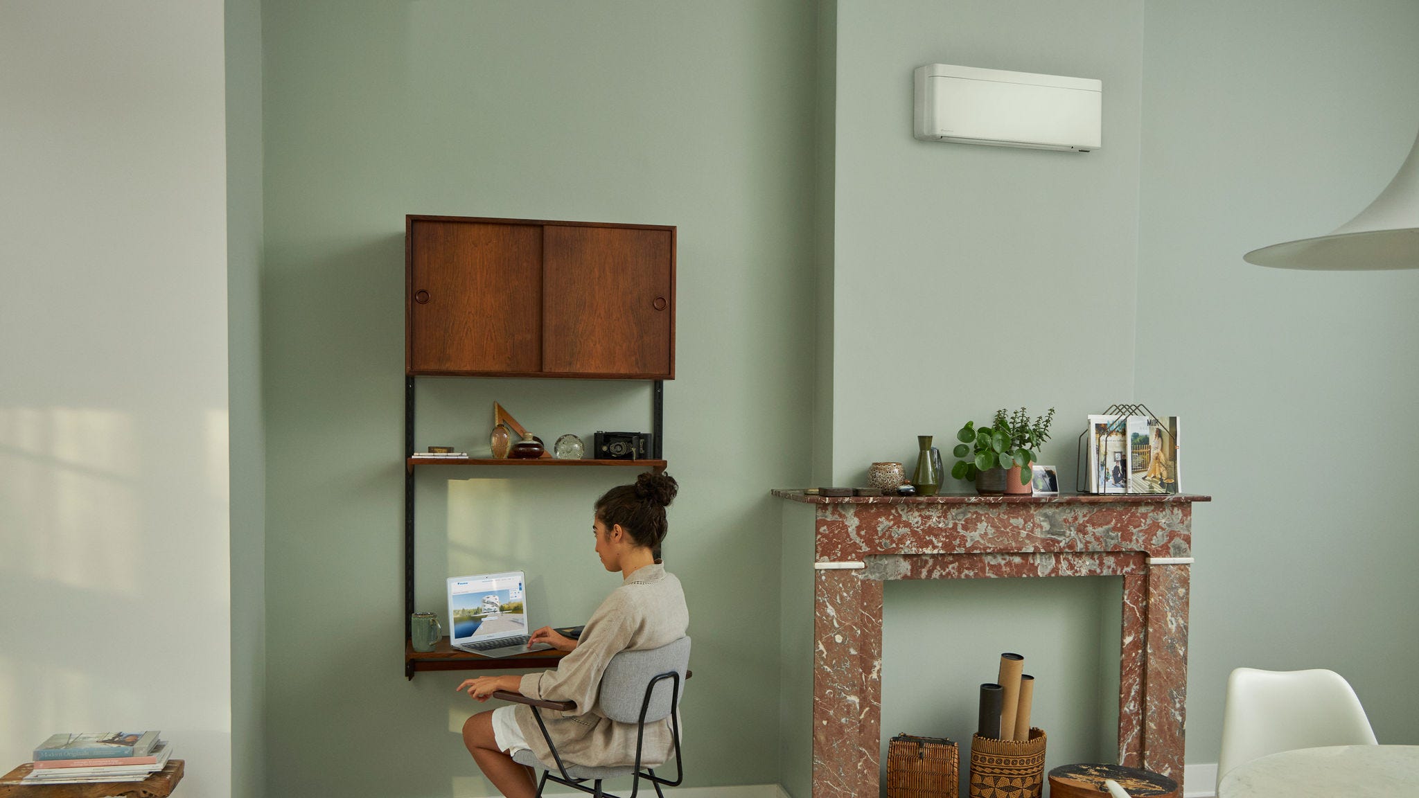 Femeie care vizitează Centrul de Experiență Virtuală Daikin prin intermediul laptopului la biroul mic din camera de zi frumos decorată